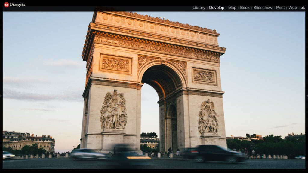 Arc de Triomphe Paris monument with intricate sculptures, captured during sunset with moving cars in foreground.